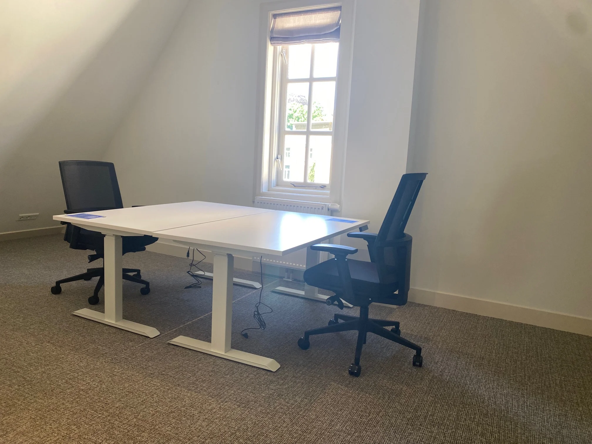 Twee bureaustoelen en een wit tweepersoonsbureau in een licht kantoor aan de Kleine Houtweg.